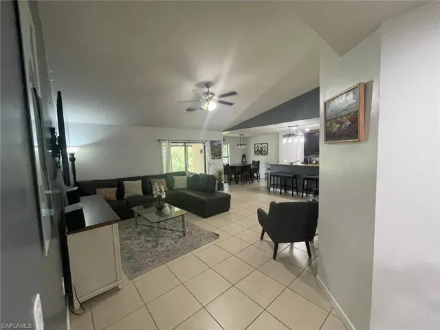 Tiled living room with ceiling fan with notable chandelier and vaulted ceiling