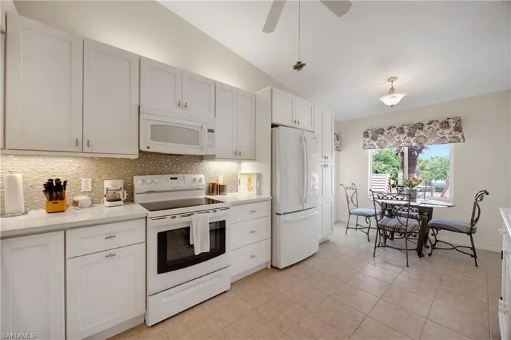 Kitchen featuring light countertops, white appliances, backsplash, and vaulted ceiling