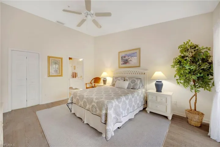 Bedroom with baseboards, visible vents, light wood-style floors, ceiling fan, and ensuite bath