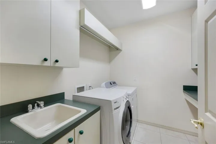 Washroom with cabinets, washing machine and dryer, light tile patterned floors, and sink