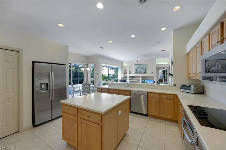 Kitchen with sink, stainless steel appliances, light brown cabinetry, a kitchen island, and ceiling fan with notable chandelier