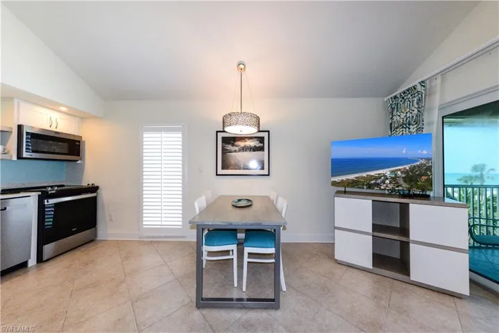 Kitchen with stainless steel appliances, vaulted ceiling, light tile patterned floors, white cabinets, and baseboards