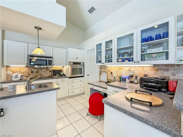 Kitchen featuring backsplash, pendant lighting, stainless steel appliances, white cabinets, and light tile patterned floors
