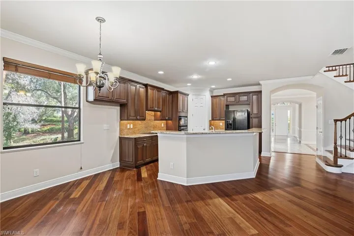 Kitchen with a chandelier over casual dining, arched walkways, black fridge, an island with sink, and tasteful backsplash