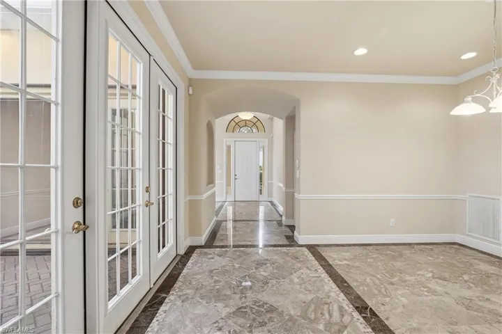 Foyer featuring arched walkways, marble tiled flooring, crown molding, french doors, and inlaid floor details