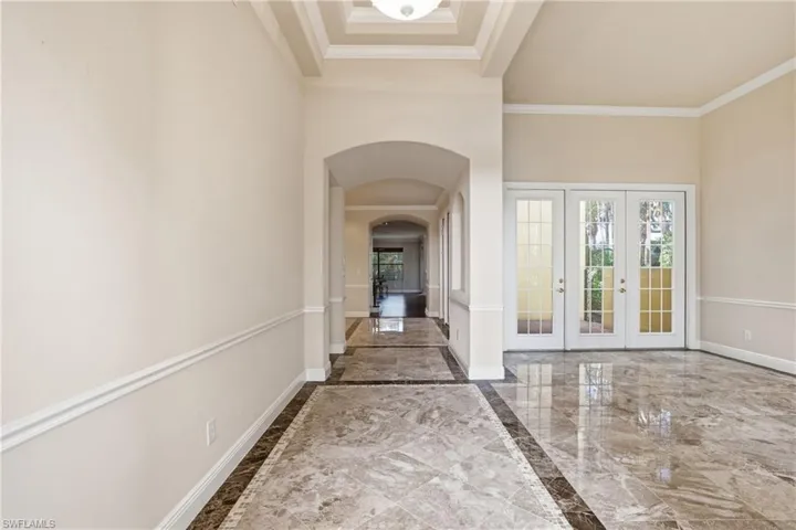 Hallway featuring light marble finish floors, arched walkways, french doors, healthy amount of natural light, and ornamental molding