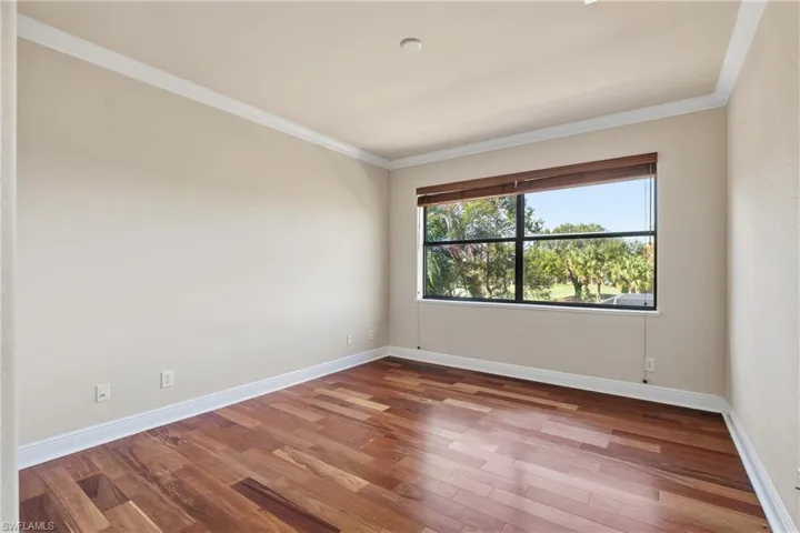 Upstairs guest bedroom featuring wood-finished flooring and ornamental molding, with picturesque views overlooking the pool and golf course.