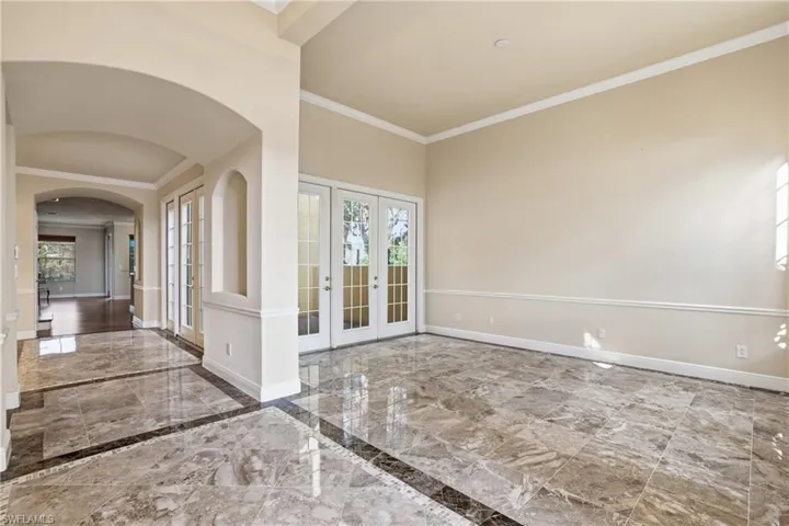 Inviting receiving and living area featuring marble tile flooring, elegant French doors, crown molding, and graceful arched walkways leading to formal dining room and kitchen.