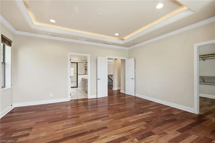 Primary bedroom with ensuite bathroom, wood-type flooring, crown molding, a raised ceiling, and recessed lighting complete with walk-in closet.