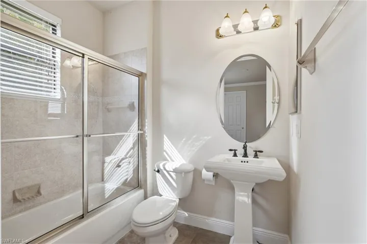 Bathroom featuring bath / shower combo with glass door and tile patterned flooring.