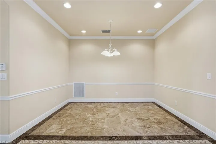Empty room featuring suspended lighting, crown molding, and inlaid floor details