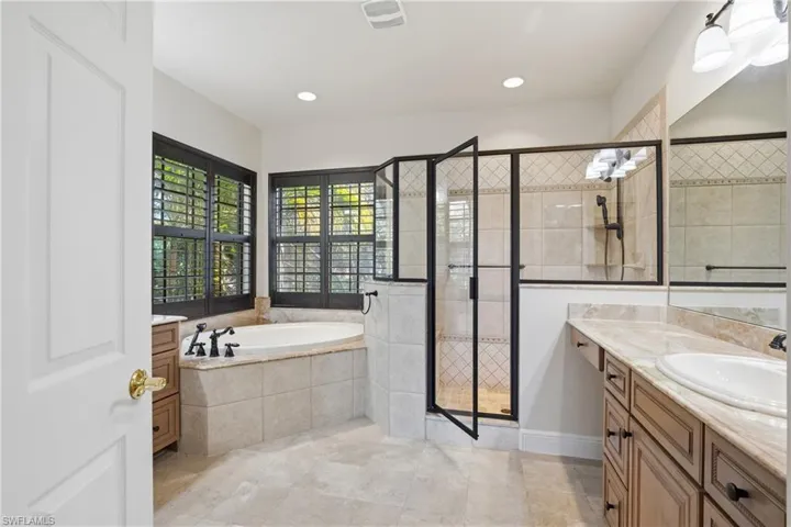 Modern primary bathroom featuring a soaking bath tub, a stall shower,  2 vanities, and recessed lighting