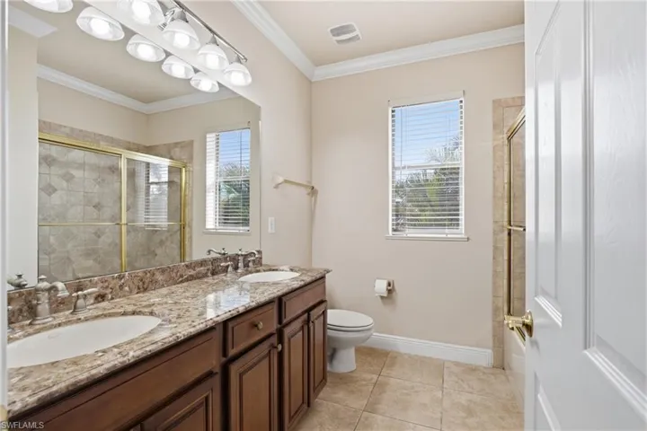 Upstairs guest bathroom with ornamental molding, double vanity, and light tile floors