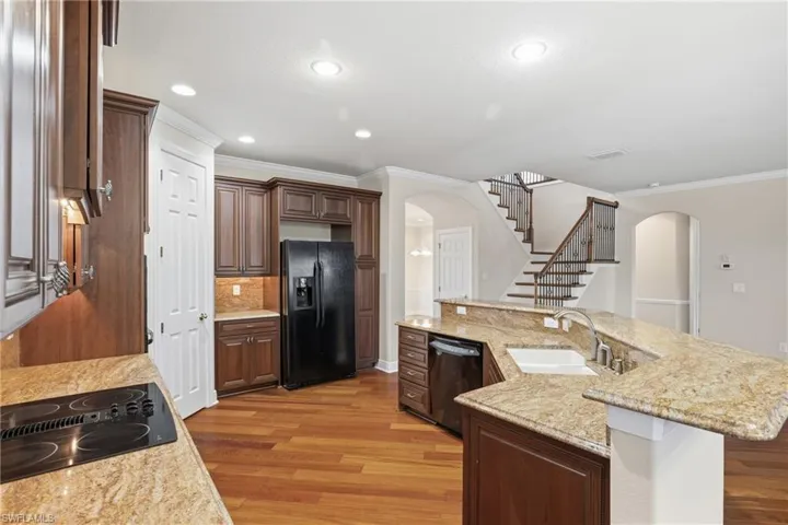 Kitchen featuring an island with sink, black appliances, crown molding, wood finish cabinets, and wood-type flooring