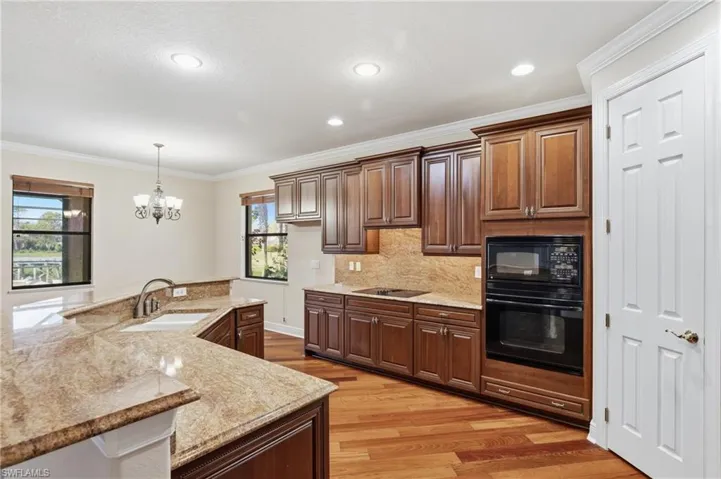 Kitchen featuring ornamental molding, suspended lighting, wood-type flooring, black appliances, and stone counters complete with pantry.