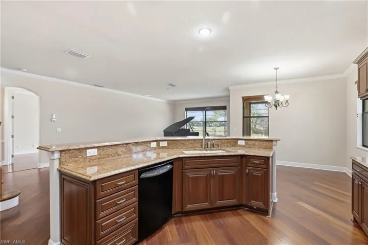Kitchen with arched walkways, dishwasher, light stone counters, dark wood-type flooring, and a chandelier