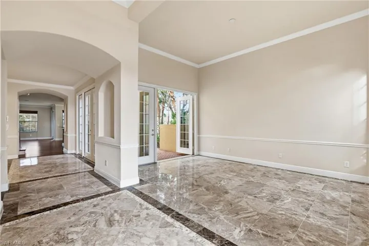 Elegant living area highlighted by crown molding, marble-finish flooring with inlaid detailing, French doors, and graceful arched walkways, all opening to a charming side patio perfect for relaxing afternoons or enjoying tea in a serene setting.