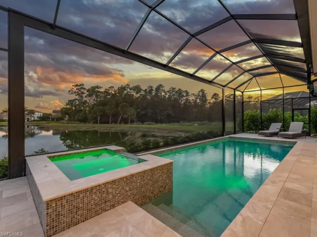 Pool at dusk featuring in ground hot tub, pool, panoramic screens and private views of the lake and preserve.