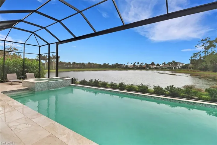 View of pool with glass enclosure, a water view, and an in ground hot tub