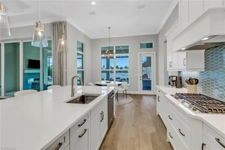Kitchen featuring light hardwood floors, white cabinetry, decorative light fixtures and custom back splash