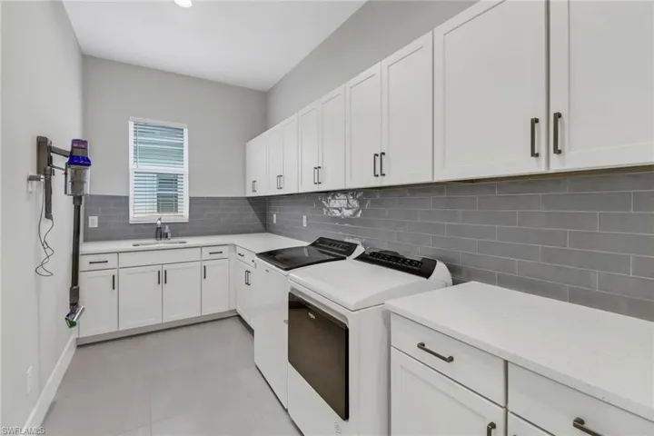 Laundry featuring washing machine and clothes dryer, white cabinets, light tile patterned floors and laundry sink.