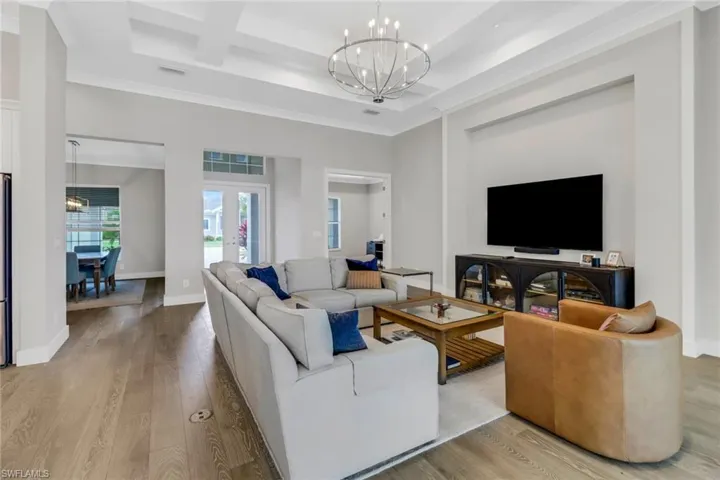 Living room featuring french doors entry, light hardwood floors, a custom chandelier, coffered ceiling.