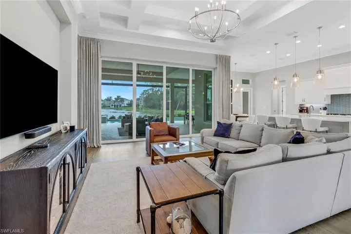 Living room with light hardwood floors, coffered ceiling inviting water view.