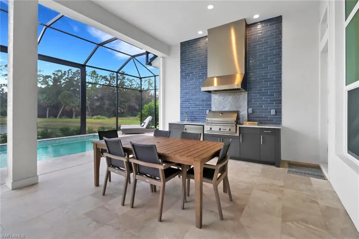 View of patio with custom outdoor kitchen includes grill, wine cooler and wet sink. Relax in the salt water pool and lake views beyond.