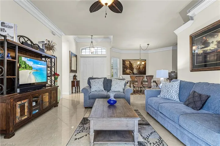 Spacious living area featuring light-colored tile flooring, crown molding, and a ceiling fan