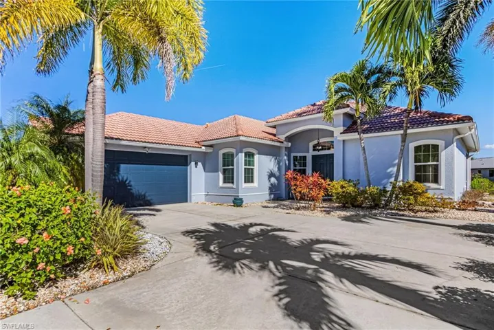 The property features a concrete driveway, a tile roof, an attached garage, and tropical landscaping with palm trees