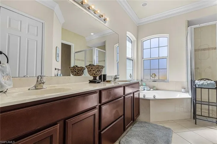 Bathroom featuring a double vanity with dark wood cabinetry and a light-colored countertop, a corner bathtub, and arched windows
