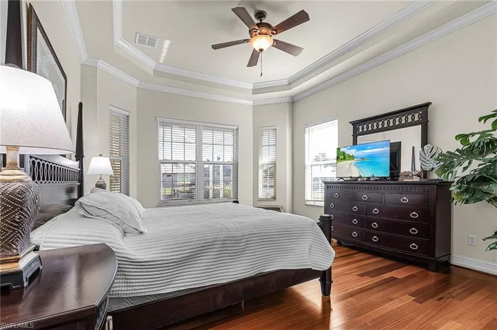 Spacious room featuring hardwood flooring, a ceiling fan, and multiple windows with blinds