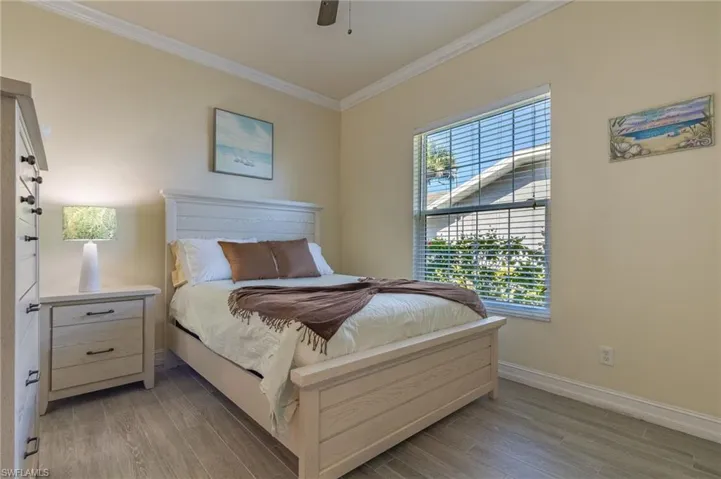 This bedroom features a light color palette, a window with blinds, and crown molding