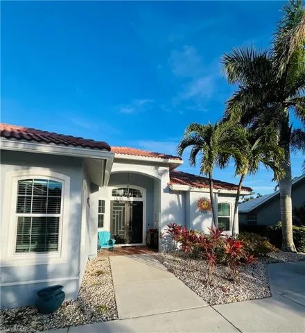 The property features a concrete walkway leading to the entrance, a well-maintained rock garden with various plantings, and mature palm trees