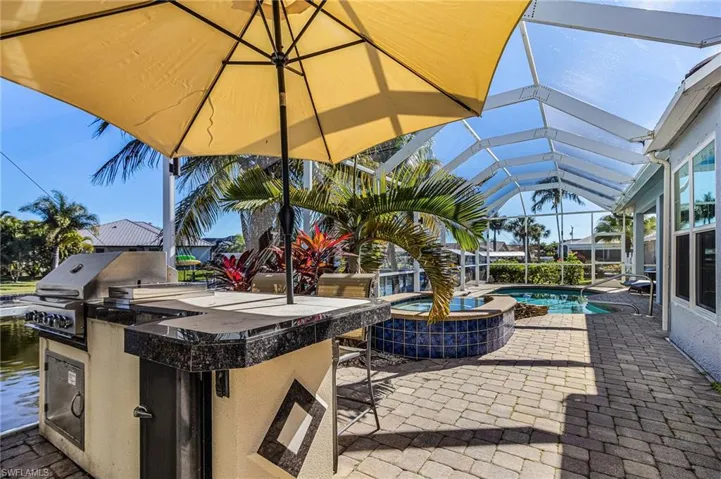 The screened lanai features a built-in outdoor kitchen with a grill and dark granite countertops, a swimming pool, and a tiled spa
