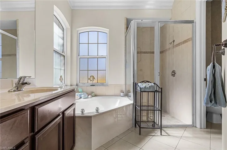 Bathroom featuring a corner soaking tub, a separate glass-enclosed shower, a vanity with a light-colored countertop, and two arched windows