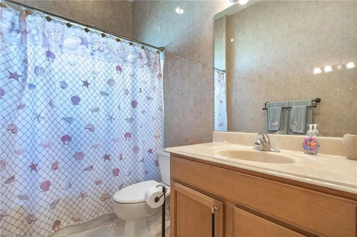 The bathroom features a light-colored vanity with an integrated sink, a large mirror, and tiled walls