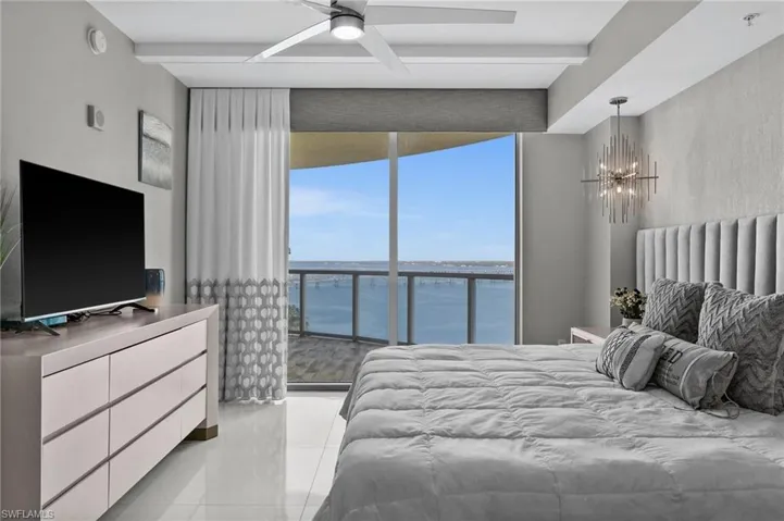 What a Primary Master Bedroom with modern lighting, a notable chandelier, a water view, beam ceiling, and light tile patterned floors