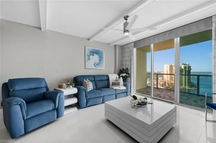 Tiled living room with a water view, beamed ceiling, and ceiling fan