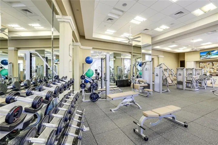 Gym featuring decorative columns, ceiling fan, and a drop ceiling