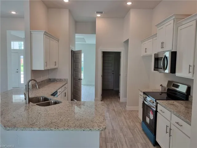 Kitchen featuring light stone countertops, light hardwood / wood-style floors, stainless steel appliances, sink, and kitchen peninsula