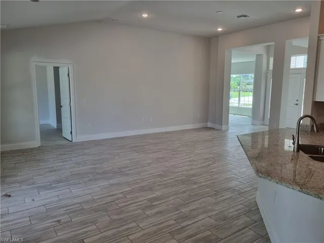 Unfurnished living room with light wood-type flooring, lofted ceiling, and sink