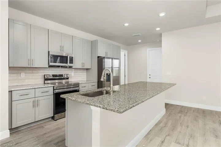 Kitchen featuring appliances with stainless steel finishes, a center island with sink, light stone counters, and sink, finishes may vary.