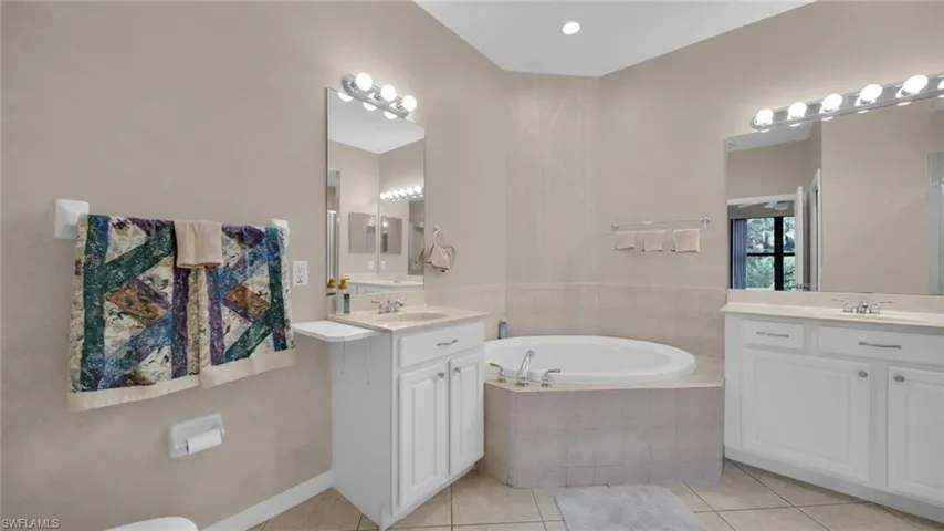 Bathroom featuring light tile patterned floors, a garden tub, two vanities, and recessed lighting