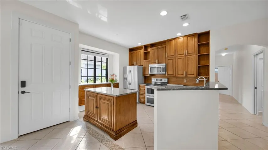 Kitchen featuring brown cabinets, open shelves, light tile patterned flooring, appliances with stainless steel finishes, and dark stone counters