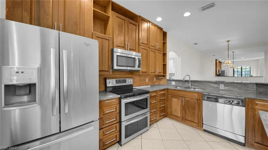 Kitchen with open shelves, stainless steel appliances, brown cabinets, recessed lighting, and decorative light fixtures