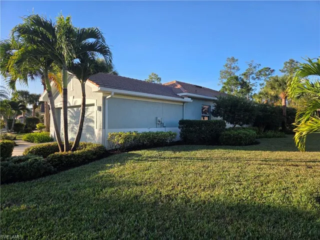 View of side of home featuring a garage, stucco siding, a lawn, and a tiled roof