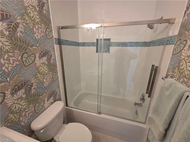 Bathroom with shower / bath combination with glass door and wallpapered walls