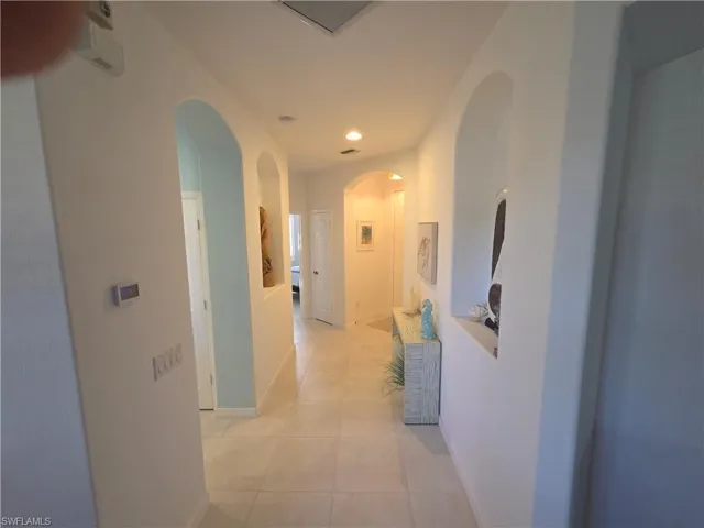 Hallway with light tile patterned floors, recessed lighting, and arched walkways