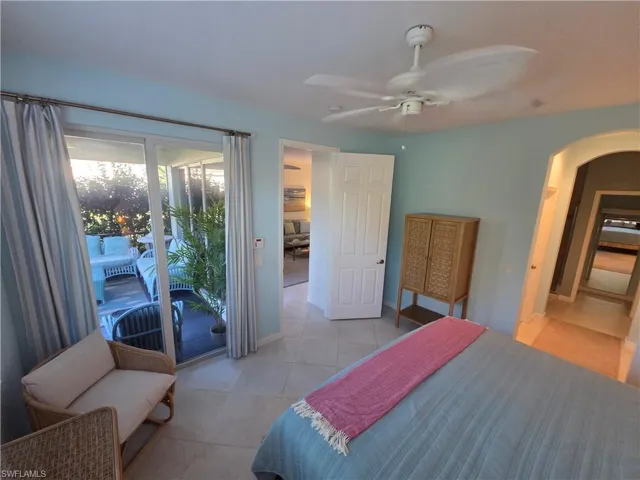 Bedroom with arched walkways, access to outside, light tile patterned flooring, and a ceiling fan